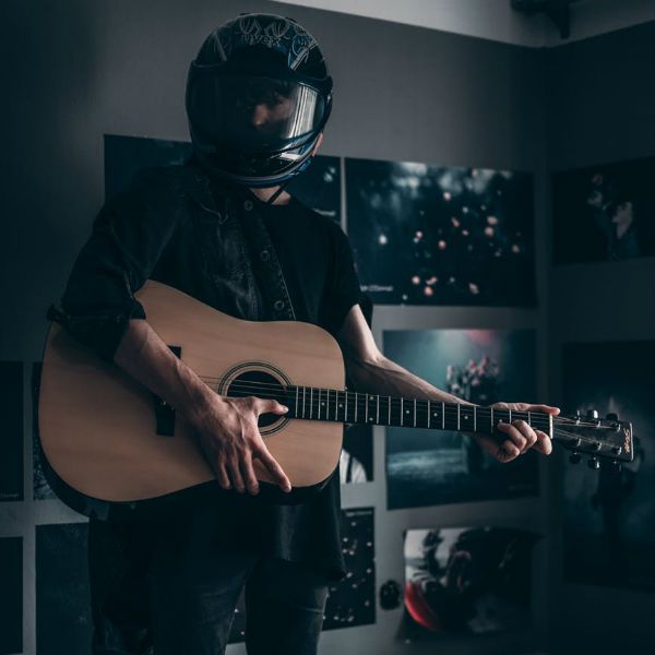 Músico usa capacete, botas e segura seu violão