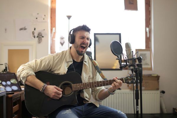 Músico toca violão e canta, em um home studio