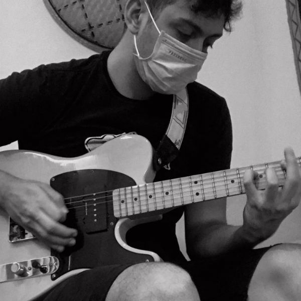 Jovem músico toca guitarra e usa máscara de proteção contra o coronavírus