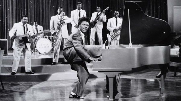 Um jovem Little Richard tocando piano e com uma das pernas sobre o instrumento