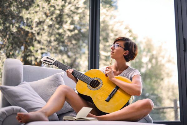 Mulher toca violão sentada no sofá