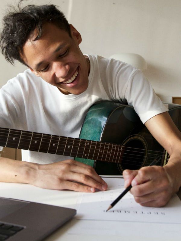 Com violão no colo, jovem músico anota cifras de música que pretende enviar para o CIfra Club