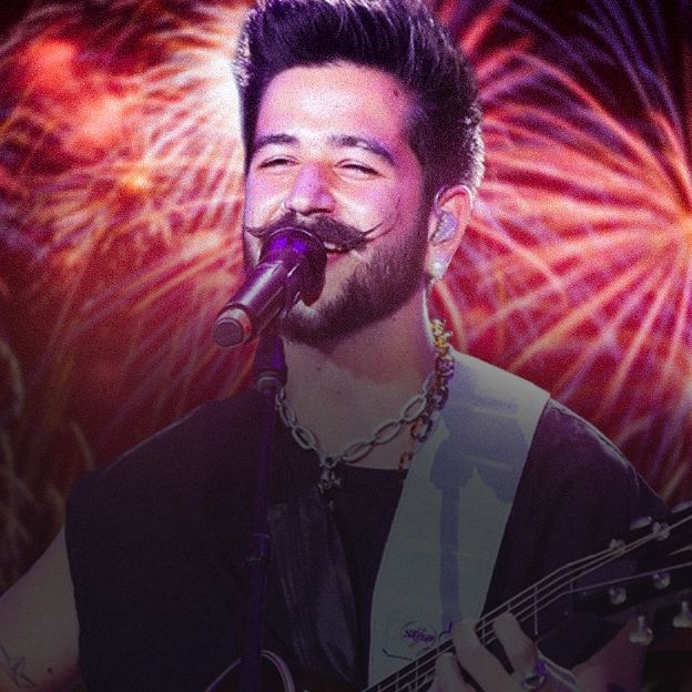 En la imagen el cantante Camilo canta, y de fondo fuegos artificiales.