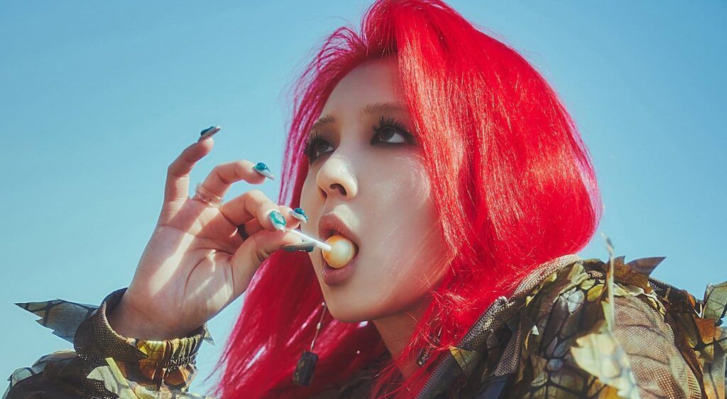 En la imagen, está Jiwoo sosteniendo un chupetín en la boca