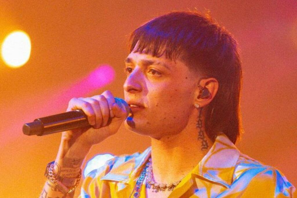 En la imagen, está Peso Pluma cantando durante un concierto