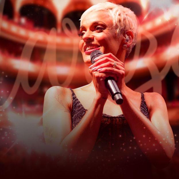 Cantora Mariza posa no centro da imagem com um microfone na mão