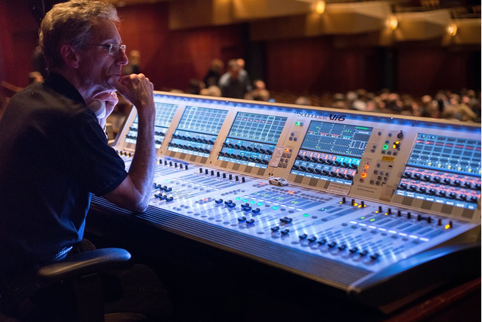 Técnico de áudio diante de uma mderna mesa de som, controlando a sonorização de um teatro