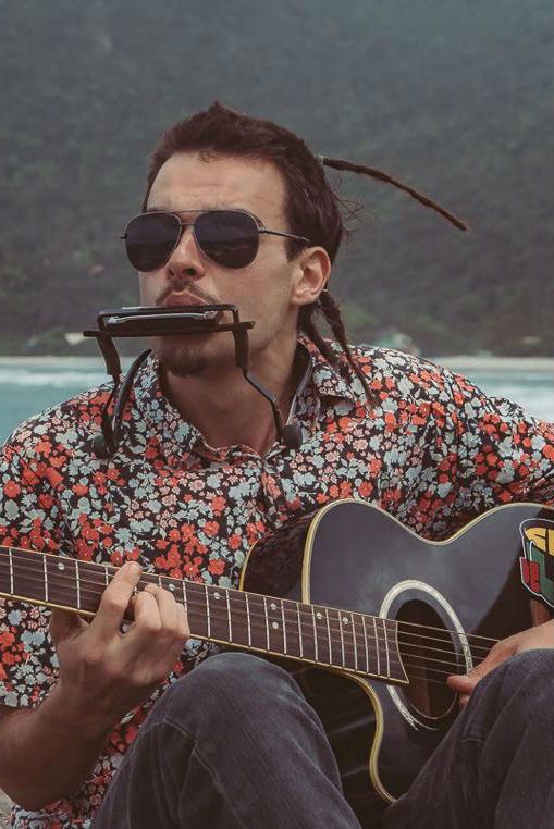 De costas para o mar, Lucas Plant toca violão e gaita