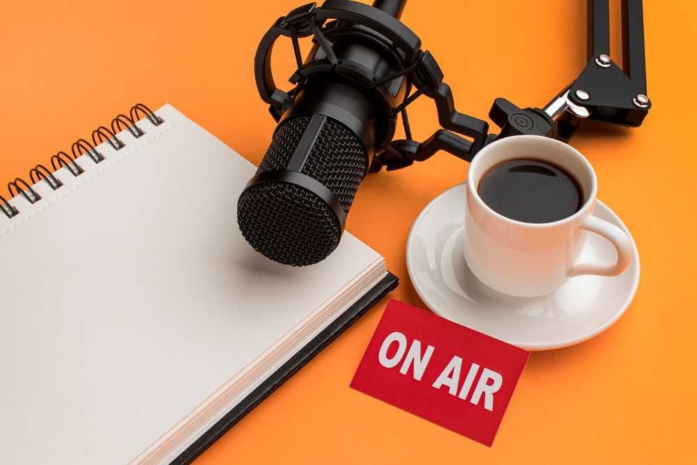 Mesa laranja com um cafézinho, um microfone de podcast e um caderno